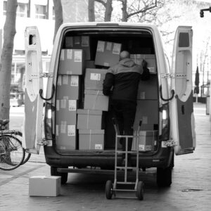 Monochrome image of a man loading packages into a van outdoors in the Netherlands.